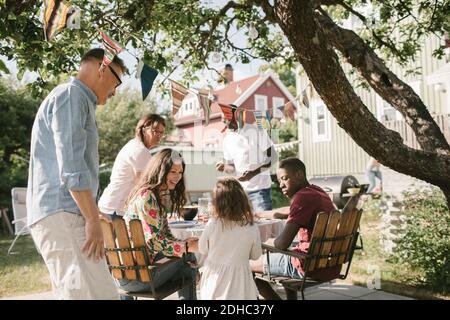 Famiglia che guarda la ragazza in piedi al tavolo in cortile durante festa in giardino Foto Stock
