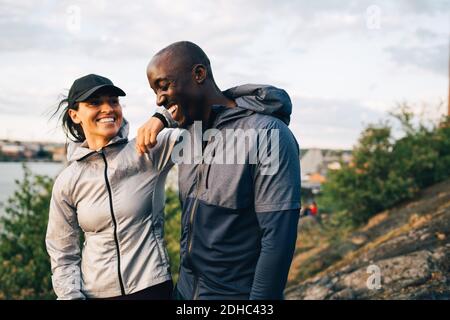 Atleta sorridente di sesso maschile e femminile in piedi in collina contro il cielo Foto Stock