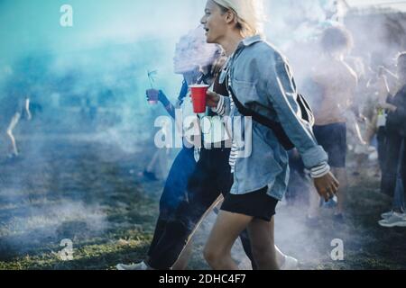 Gli amici gustano un drink mentre camminano con la vernice a polvere amista in festival Foto Stock