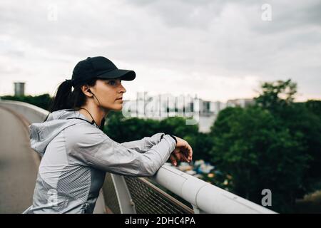 Donna sportiva stanca che guarda via mentre si appoggia sulla ringhiera al ponte pedonale in città Foto Stock