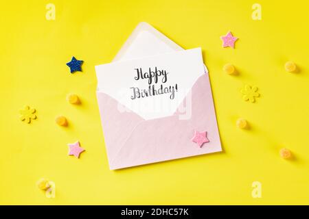 Cartolina happy Birthday scritta a mano in una busta rosa, con un colpo superiore su sfondo giallo Foto Stock