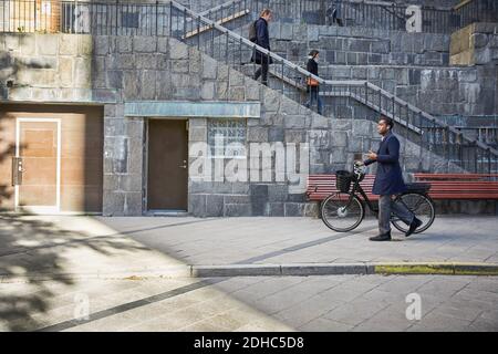 Vista laterale completa dell'uomo che cammina con una bicicletta elettrica sul sentiero in città Foto Stock