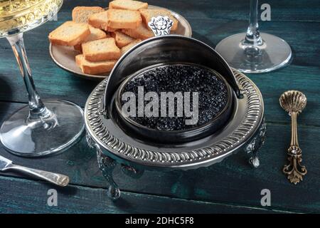 Caviale nero in una ciotola vintage, con cucchiaio e pane, su fondo di legno scuro Foto Stock