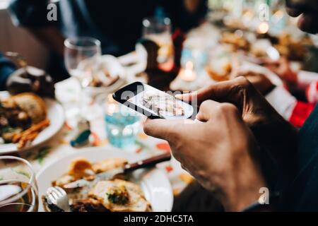 Immagine ritagliata di giovane uomo che fotografa il cibo in piatto a. ristorante Foto Stock