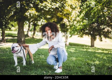 Ritratto di donna sorridente con bulldog su campo erboso a. parcheggio Foto Stock