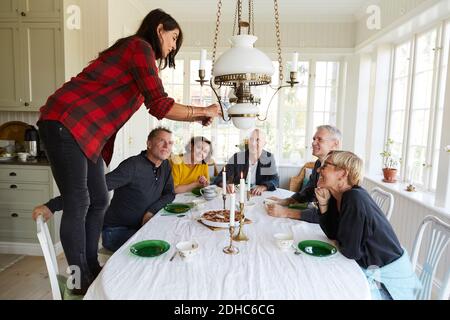 Amici che guardano una donna che fotografa il cibo sul tavolo da pranzo a. casa Foto Stock