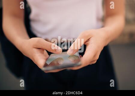 La sezione centrale della messaggistica di testo di giovane donna attraverso il telefono cellulare in città Foto Stock