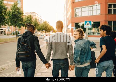 Vista posteriore degli amici maschi che camminano fianco a fianco via in città Foto Stock