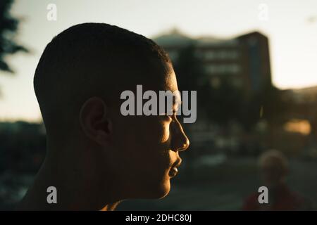 Vista laterale di un adolescente attento che guarda lontano in città durante il tramonto Foto Stock