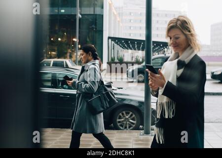 Uomini d'affari che usano smartphone mentre camminano sul marciapiede in città Foto Stock