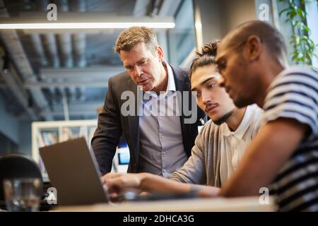 Imprenditori maschili che discutono con il responsabile della banca sopra il laptop alla scrivania in ufficio creativo Foto Stock