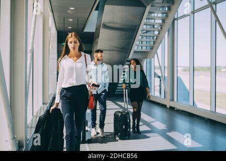 Giovane donna d'affari che cammina di fronte ai colleghi nel corridoio a. aeroporto Foto Stock
