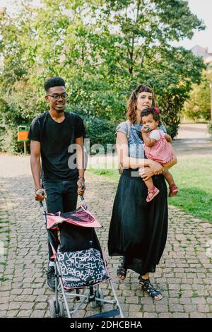 Donna che porta la figlia mentre l'uomo spinge il passeggino del bambino sul sentiero nel parco Foto Stock