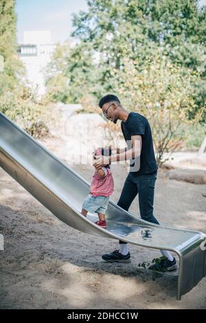 Giovane uomo che tiene le mani di figlia che cammina sullo scivolo a. parco giochi Foto Stock