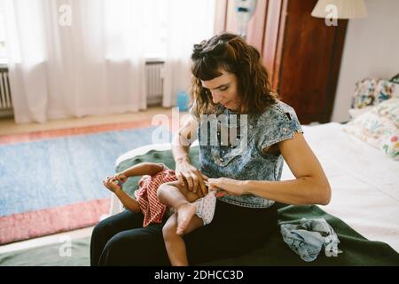 Madre che regola il pannolino di figlia mentre si siede sul letto a. casa Foto Stock