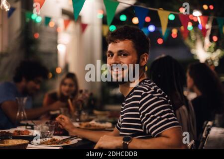 Ritratto di giovane sorridente che cena con gli amici durante festa in giardino Foto Stock