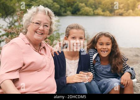 Ritratto di nipoti sorridenti e nonna seduta sul lakeshore dentro parcheggio Foto Stock