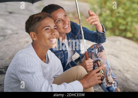 Sorridi madre e figlio che guardano in su mentre condividono l'ombrello dentro parcheggio Foto Stock