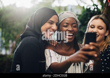 Sorridendo amici multietnici che prendono selfie tramite telefono cellulare in cortile Foto Stock