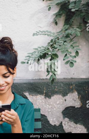 Immagine ritagliata di una giovane donna che usa il telefono cellulare contro la parete Foto Stock