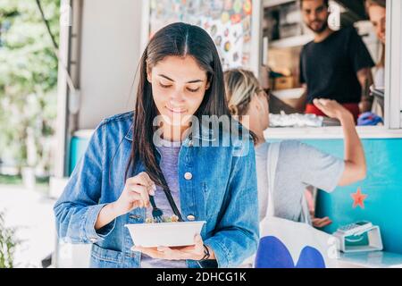 Giovane donna che mangia Tex-Mex fresco in ciotola contro camion di cibo Foto Stock