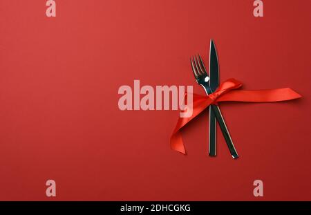 Piatto rotondo e forchetta in metallo e coltello legati con un nastro di seta rossa, fondo di legno blu Foto Stock