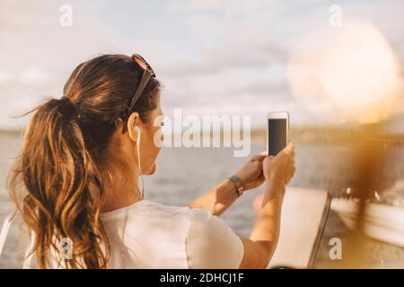 Donna che prende selfie attraverso il telefono cellulare contro il lago durante l'estate vacanza Foto Stock