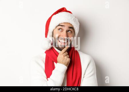 Festa di Capodanno e concetto di vacanza invernale. Primo piano di bell'uomo bearded che osserva pensieroso, che progetta la lista del regalo di Natale dentro Foto Stock