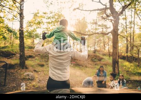 Uomo che porta le spalle del figlio durante il picnic con la famiglia in pubblico parcheggio Foto Stock