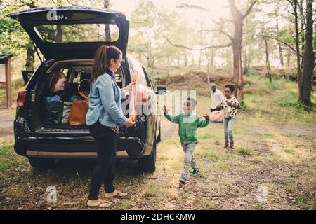 Bambini che aiutano la madre a scaricare i bagagli dal bagagliaio dell'auto al pubblico parcheggio Foto Stock