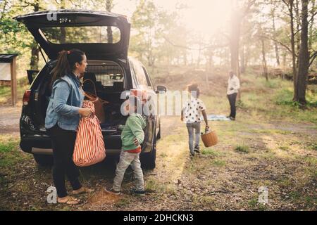 La famiglia scarica i bagagli dal bagagliaio dell'auto elettrica al parcheggio Foto Stock