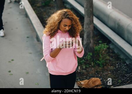 Visualizzazione ad alto angolo della messaggistica di testo femminile sul telefono cellulare presso il parco skateboard Foto Stock