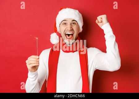 Concetto di natale, vacanze invernali e celebrazione. Ritratto di un bell'uomo eccitato, alzando la mano e tenendo sparkler, w Foto Stock