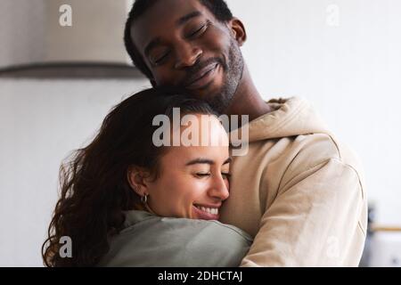 Amando giovane coppia di etnia mista coccolarsi mentre si sta in cucina insieme Foto Stock
