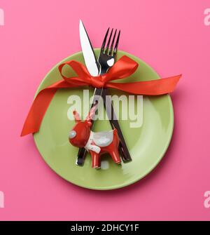 Piatto rotondo e forchetta in metallo e coltello legati con un nastro di seta rossa, fondo di legno blu Foto Stock