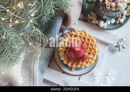 cialde viennesi con lamponi e miele sul tavolo di natale con rami di alberi di natale e ghirlande di luci sullo sfondo. vista dall'alto . Foto Stock