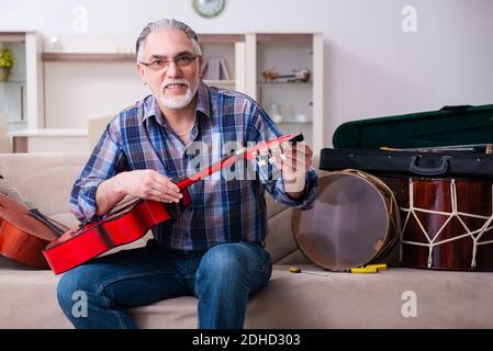 Uomo di riparazione senior che ripara gli strumenti musicali a casa Foto Stock