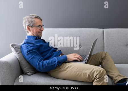 Uomo che usa il computer portatile seduto sul divano a casa Foto Stock