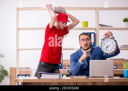 Giovane uomo che consegna la pizza in ufficio in gestione del tempo conc Foto Stock