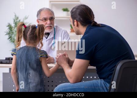 Giovane padre e sua figlia in visita al vecchio medico maschile Foto Stock