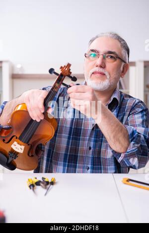 Uomo di riparazione senior che ripara gli strumenti musicali a casa Foto Stock