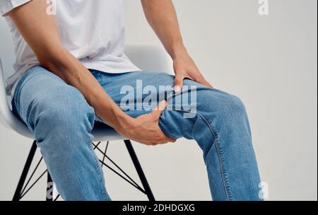 uomo in jeans seduto su una sedia e toccandolo gamba con le mani vista tagliata Foto Stock