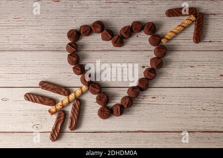 Immagine piatta dei tartufi di cioccolato disegnati a forma di cuore con una freccia fatta di biscotti che lo attraversano. Un concetto dolce e delizioso Foto Stock
