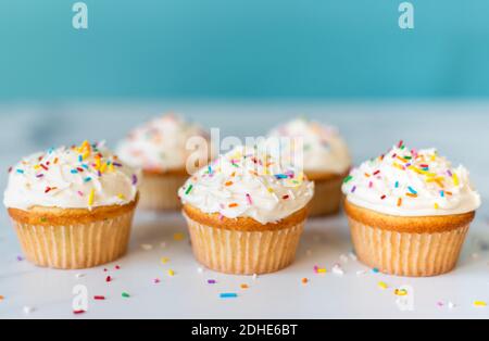 Cupcake con spruzzini su tavola bianca con sfondo blu. Foto Stock