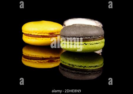 Macaroni colorati (macaron) isolati sullo sfondo nero riflettente. Dessert francese tradizionale Foto Stock