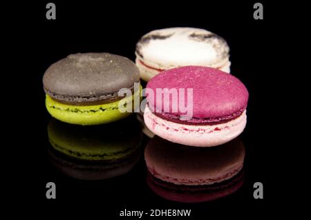 Macaroni colorati (macaron) isolati sullo sfondo nero riflettente. Dessert francese tradizionale Foto Stock