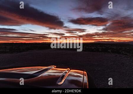 L'alba vibrante del deserto si riflette sul cofano del veicolo parcheggiato Foto Stock