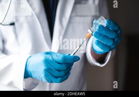 Medico in camice bianco che aspira il vaccino in una siringa per iniezione. Foto Stock