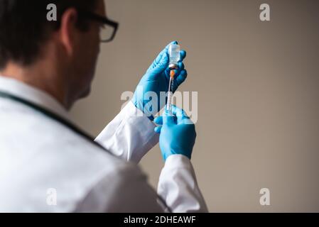 Medico in camice bianco che aspira il vaccino in una siringa per iniezione. Foto Stock