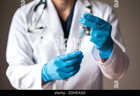 Medico in camice bianco che aspira il vaccino in una siringa per iniezione. Foto Stock